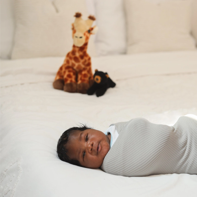 A swaddled baby with a stuffed animal in the background