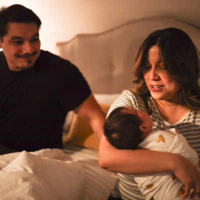 A dad watches a mom holding a baby in a bedroom